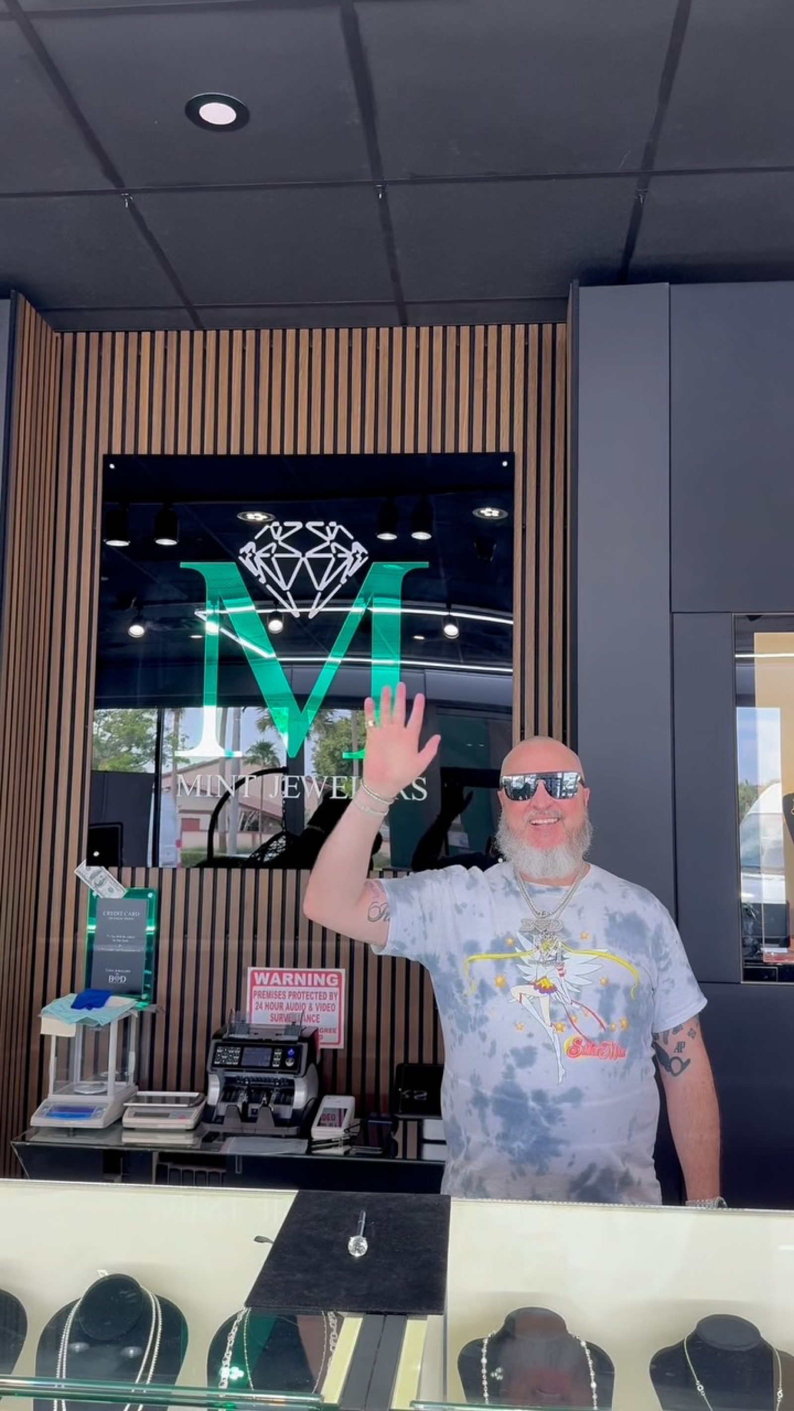Boodaddy waving outside the Mint Jewelers storefront under the green M sign