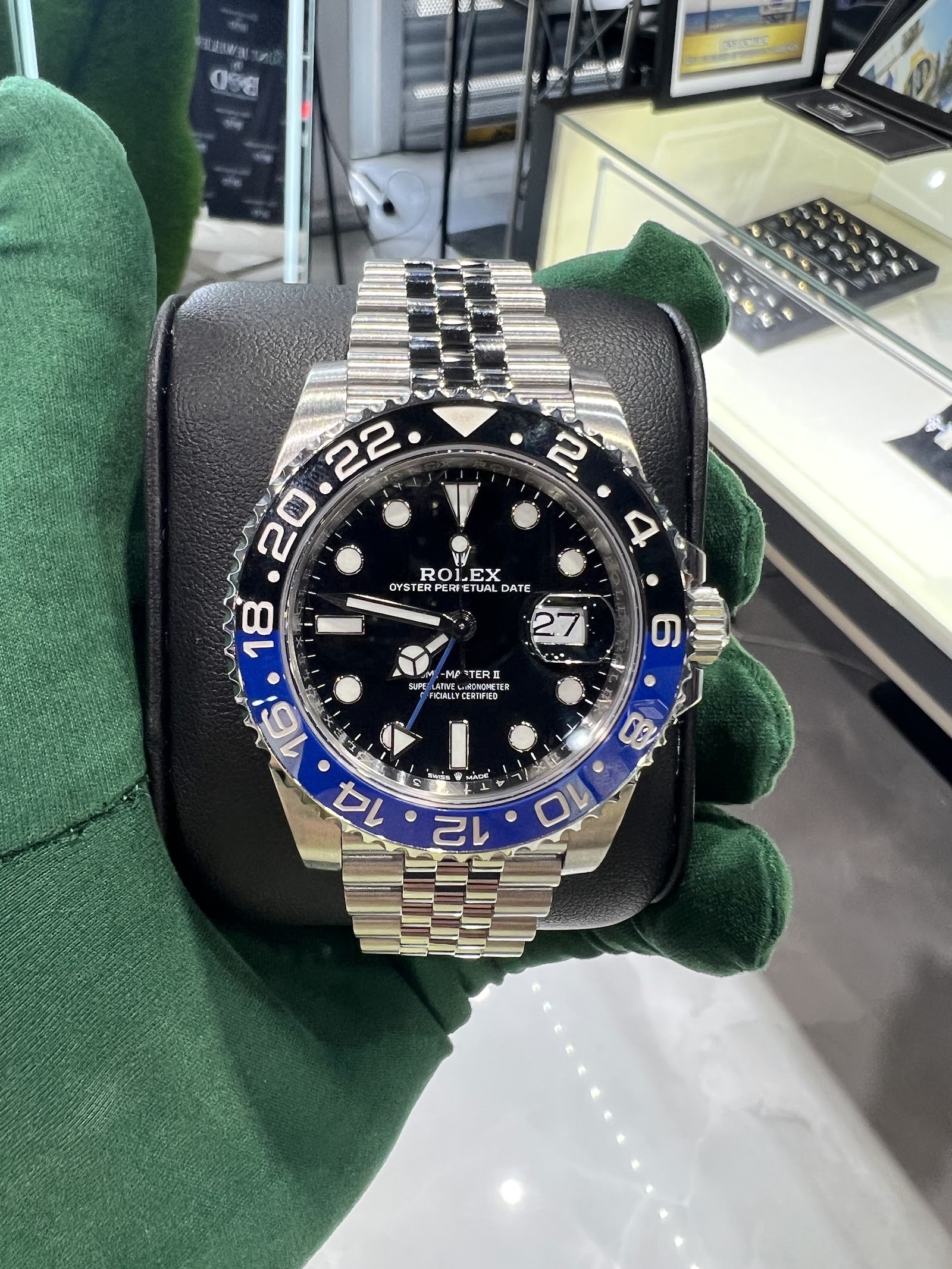 A Rolex GMT-Master II with a blue and black bezel held in a green glove at Mint Jewelers